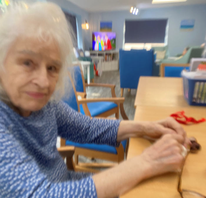 elderly woman crafting in a bright room with colorful decor and television showing animated characters engaging in creative activities