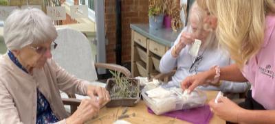 three people engaged in crafting activity with natural materials creating two handmade items on a wooden table